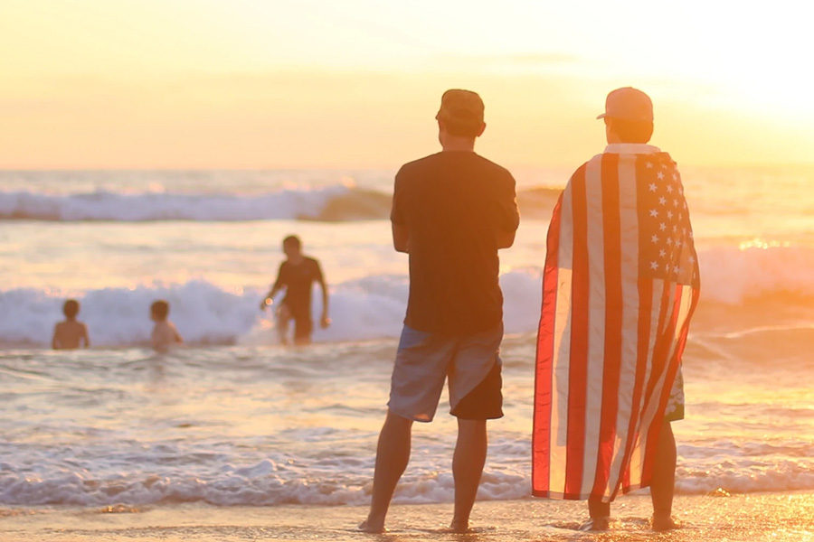 men standing on beach with American flag cape