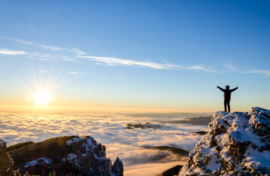 person standing at top of mountain with sunrise